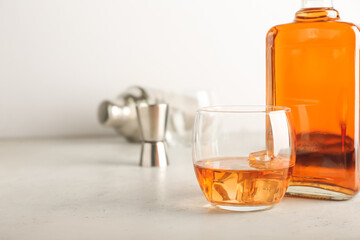 Bottle and glass of cold whiskey on light background