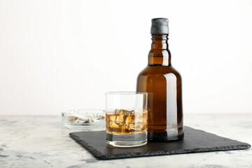 Bottle and glass of cold whiskey on light background