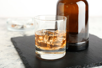 Bottle and glass of cold whiskey on light background