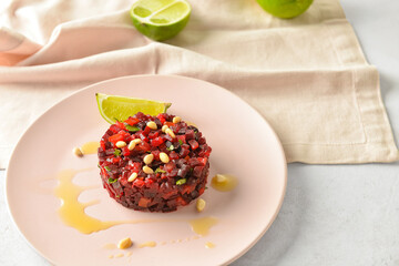 Plate with tasty tartare salad and lime on light background