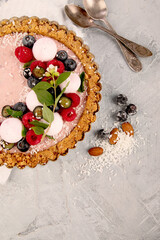 Strawberry vanila tart topped with berries on light gray background.