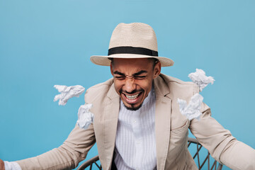Guy sits on chair and nervously scatters crumpled sheets. Portrait of man in hat and beige suit...