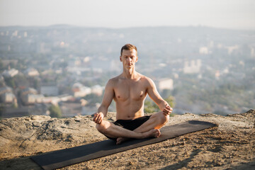 Fototapeta na wymiar Peaceful shirtless man sitting on yoga mat and practicing lotus pose with closed eyes. Concept of people, sport activity and nature.