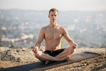 Naklejka na ściany i meble Peaceful relaxed shirtless man sitting on yoga mat in lotus asana and practicing yoga and mindfullness techniques. Concept of people, sport activity and nature.