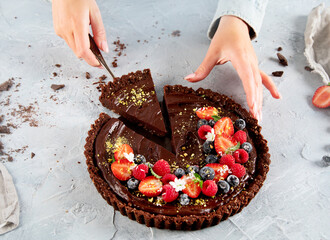 Young woman holding homemade chocolate tart on light gray background.