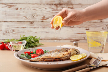 Woman squeezing lemon juice onto fried dorado on plate, closeup