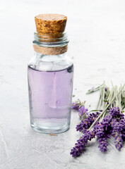 Bottle of essential oil and lavender flowers on light gray background.