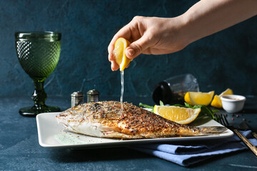 Woman squeezing lemon juice onto fried dorado on plate, closeup