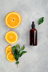 Bottle of essential aroma oil with oranges and leaves on light gray background.