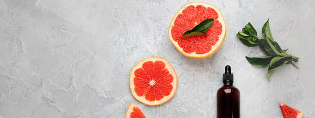 Bottle of essential aroma oil with grapefruit and leaves on light gray background.