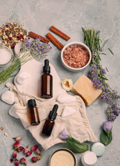 Bottle of essential oils with herbs and flowers on light gray background.