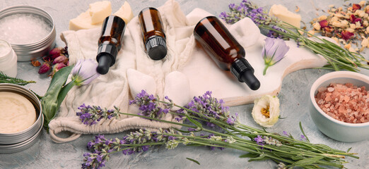 Bottle of essential oils with herbs and flowers on light gray background.