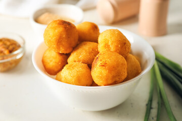 Bowl with fried potato balls on light background