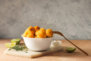 Bowl with fried potato balls and sauce on table
