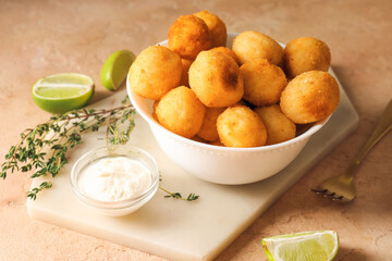 Bowl with fried potato balls and sauce on color background
