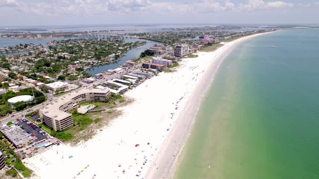 Drone shot of Saint Pete Beach Florida in the summer time. Shot runs along the beach over swimmers showing the town as well as hotels and condos. features green calm water and white sand beach.