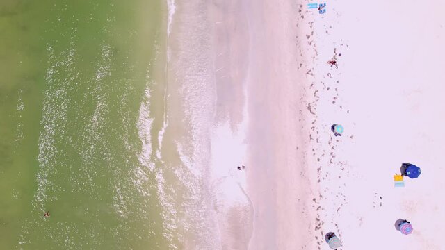Drone shot of Saint Pete Beach Florida in the summertime. Shot runs along the beach over swimmers showing the town as well as hotels and condos. features green calm water and white sand beach.
