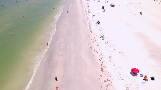 Drone shot of Saint Pete Beach Florida in the summertime. Shot runs along the beach over swimmers showing the town as well as hotels and condos. features green calm water and white sand beach.