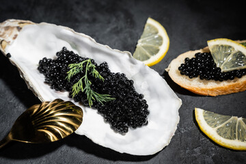 Black caviar with lemon slices on a black wooden table. The golden spoon lies nearby. Delicious delicacies. Rich food. Close-up.