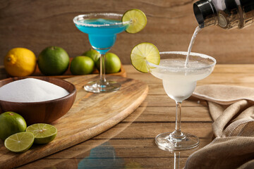 Pouring Margarita cocktail with lime and salt on wooden table background. Cocktails drink concept.