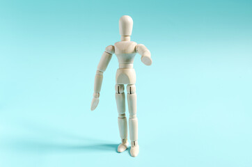 The figure of a wooden man with an outstretched arm. The figure of a wooden man on a colored background is a close-up. A wooden man and a gesture pointing with his hand
