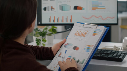 Close up of invalid disabled company director reading project documents holding clipboard checking statistics on computer with data prosessing showing on display. sitting in start up business office