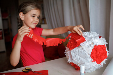 Preteen girl doing pinata with cardboard from used box and color crepe paper, decorated container...