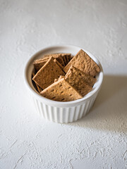 Natural flat rye mini-breads of a square shape in a white bowl on a light concrete background. Delicious and quick snack for dietary meals