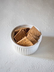 Natural flat rye mini-breads of a square shape in a white bowl on a light concrete background. Delicious and quick snack for dietary meals