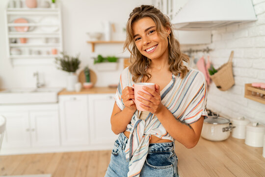 Pretty woman enjoying cozy morning on her stylish kitchen while drinking hot tea.