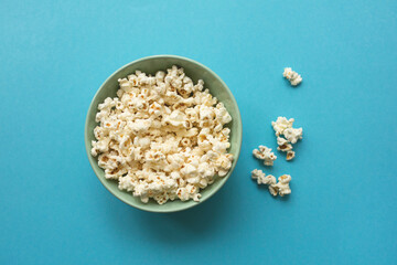 Popcorn in ceramic bowl on blue background. Top view, flat lay.