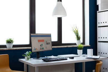 Flowers surrounding computer with financial statistics and charts in empty office. Stylish space in corporate workspace indorsors with nobody in. Company interior with professional design.