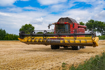 Fototapeta premium Huge red combine working in the field. Big agricultural farming equipment.