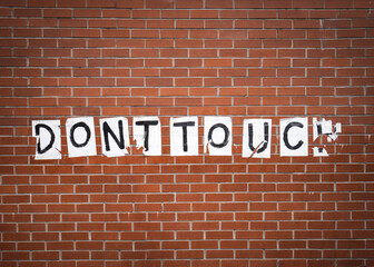 Fototapeta premium Do not Dont touch message on red brick building wall concept. Message sign ripped and torn stuck onto textured background. 