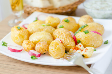 Baked young potato and redishes on a white plate. With coup of tartar souce, bread and glass of bear in blurred bokeh background.