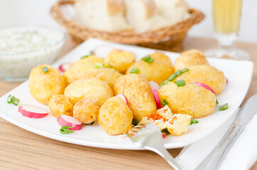 Baked young potato and redishes on a white plate. With coup of tartar souce, bread and glass of bear in blurred bokeh background.