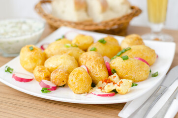 Baked young potato and redishes on a white plate. With coup of tartar souce, bread and glass of bear in blurred bokeh background.