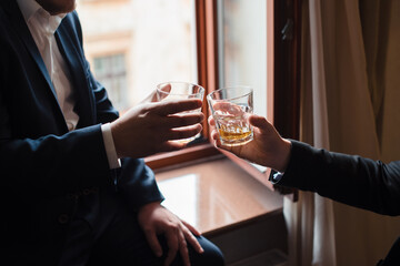 Close up of two hands of men in suits clink glasses of whiskey drink. Alcoholic beverage