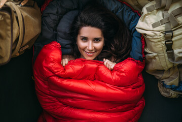 Portrait of a young woman who is cozy and warm in a red sleeping bag. Cute tourist girl with a red...