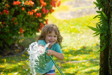 Child playing in garden, pours from the hose, makes a rain. Happy childhood concept.