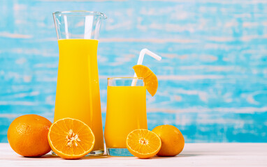 Fresh orange juice in jar and glass decorating with straw and fresh orange on white wooden table on blue wall. Studio picture concept for healthy diet