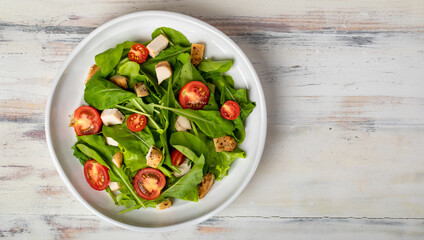 Fresh spinach salad with tomato, small pieces of herb roasted chicken in white ceramic dish on white wooded table. Concept for healthy. Studio picture