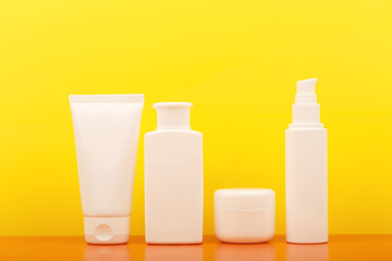 Set of white unbranded cosmetic bottles against yellow background. Concept of safe tanning, summer...