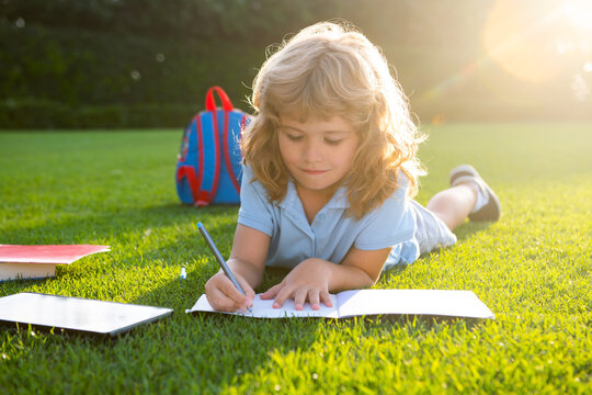 Cute childr boy with books with pencil writing on notebook outdoors. Summer camp. Kids learning and education concept. Summer vacation homework. Preschool student outdoor.