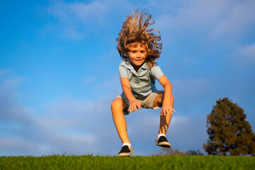 Funny redhead boy playing on the green grass in park, happy childhood. Kids active lifestyle outdoors.