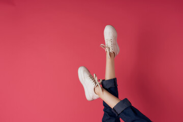 inverted female legs in white sneakers pink background cropped view studio