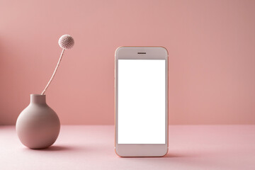 Mobile phone with white screen and dry flower in vase on pink background with dark shadows. Trend,...