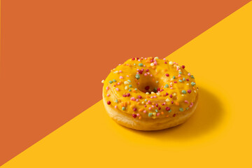 Bright donut with yellow glaze and a multi-colored sprinkle on two colour background .Sweet minimalist food image. Modern concept.