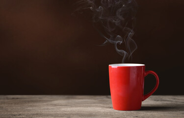Red cup of hot coffee with coffee smoke on wood.