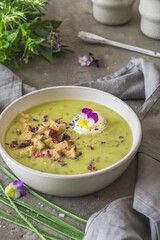 Creamy herbes soup with potatoes, herbes and sorrel, with edible blooms and croutons as topping. Gray concrete background. Vertical.